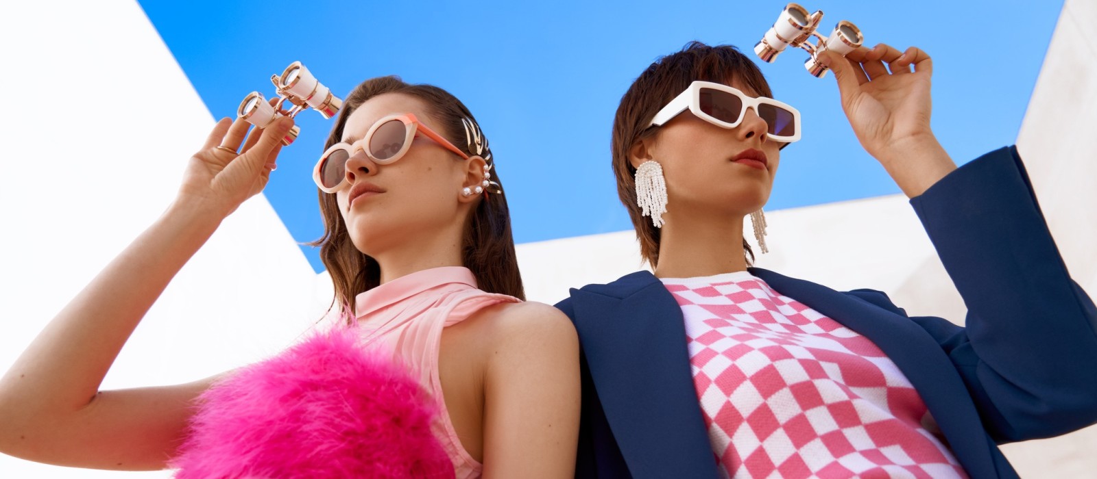 Two women wearing Woodys sunglasses, looking in opposite directions and through opera glasses.