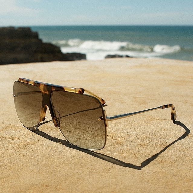 Victoria Beckham sunglasses on a beach, with waves crashing in the background