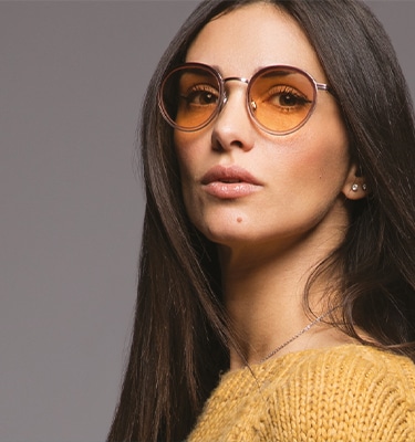 Model wearing Shamir PhotoGlamour™ lenses in brown from the Transitions® Light Intelligent Lenses™ collection, posing confidently with a serious, self-assured expression.