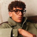 A brown-haired man with a serious, model-like expression wears Lafont. square eyeglass frames and a green army-style jacket, giving off a cool, casual October look.